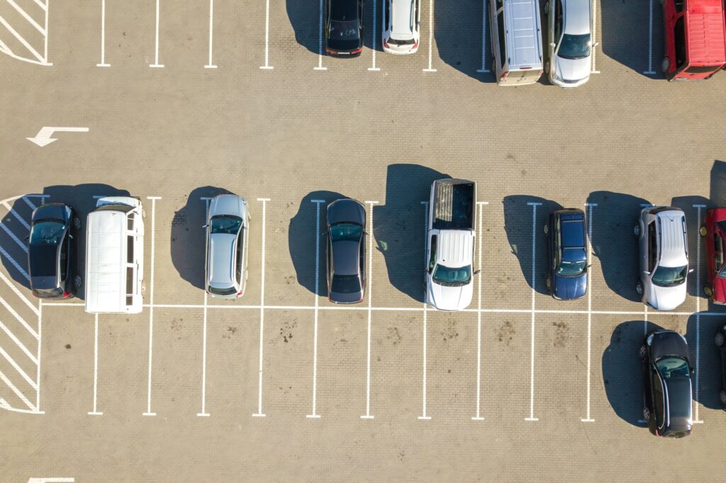 Aerial view of many colorful cars parked on parking lot with lines and markings for parking places